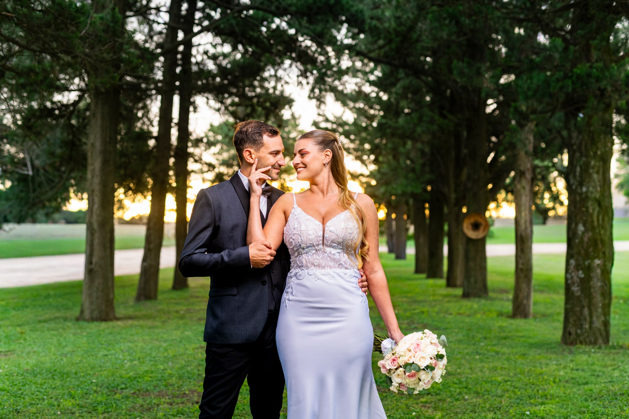 Los novios caminando entre los árboles del parque con la luz dorada del atardecer